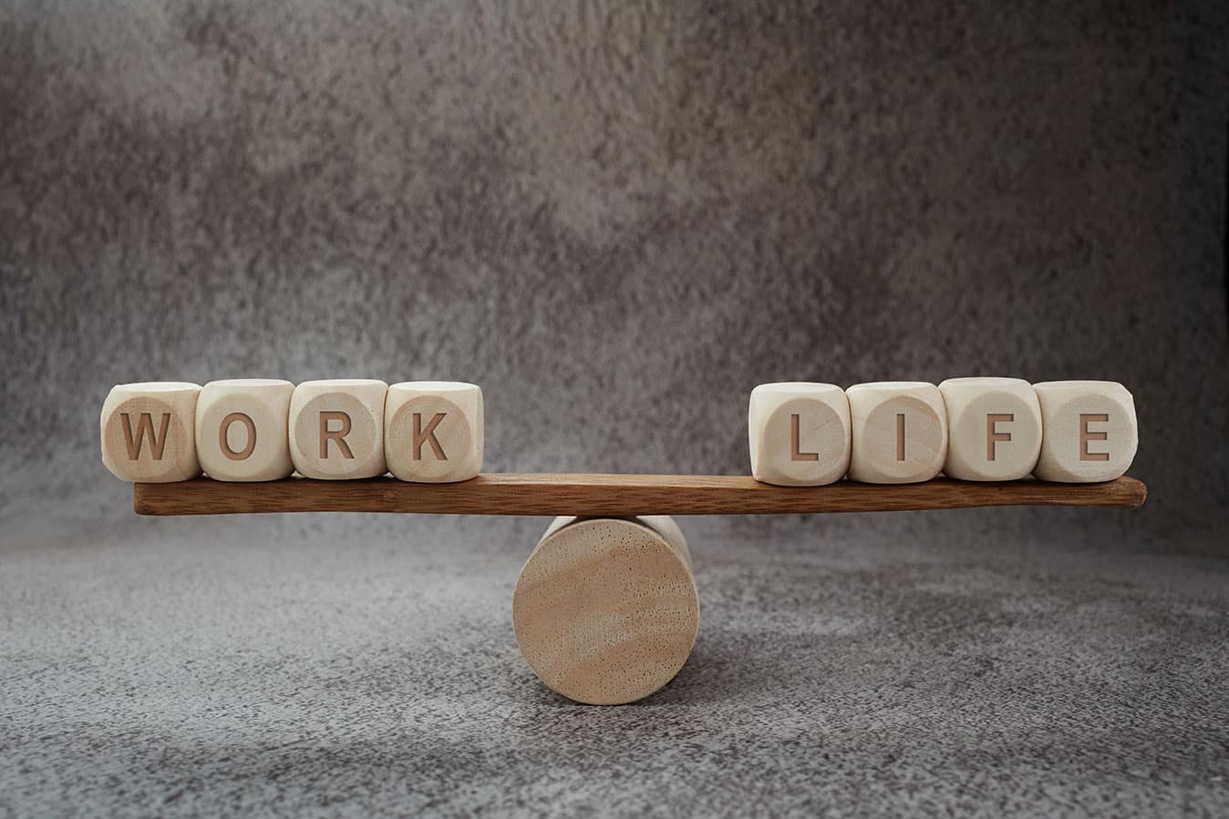 The words "work" and "life" balancing on either ends of a wooden balance scale.