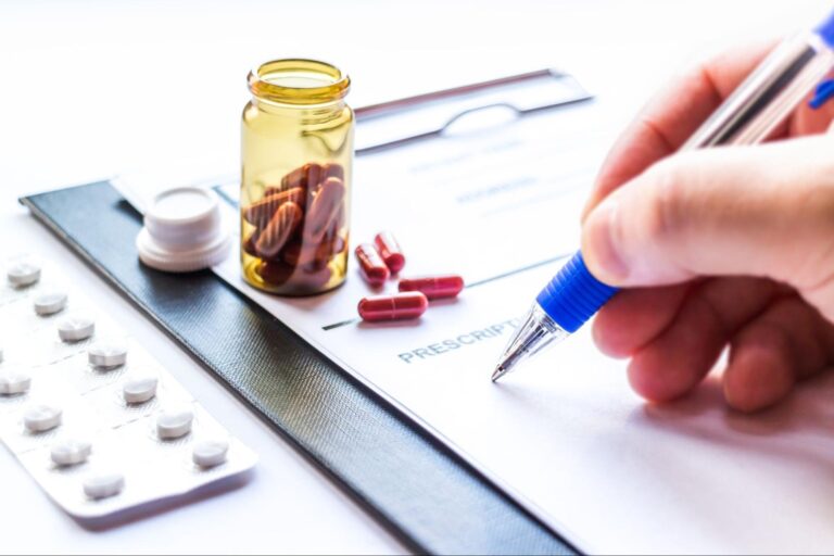 Hand writing a prescription with medicine scattered around.