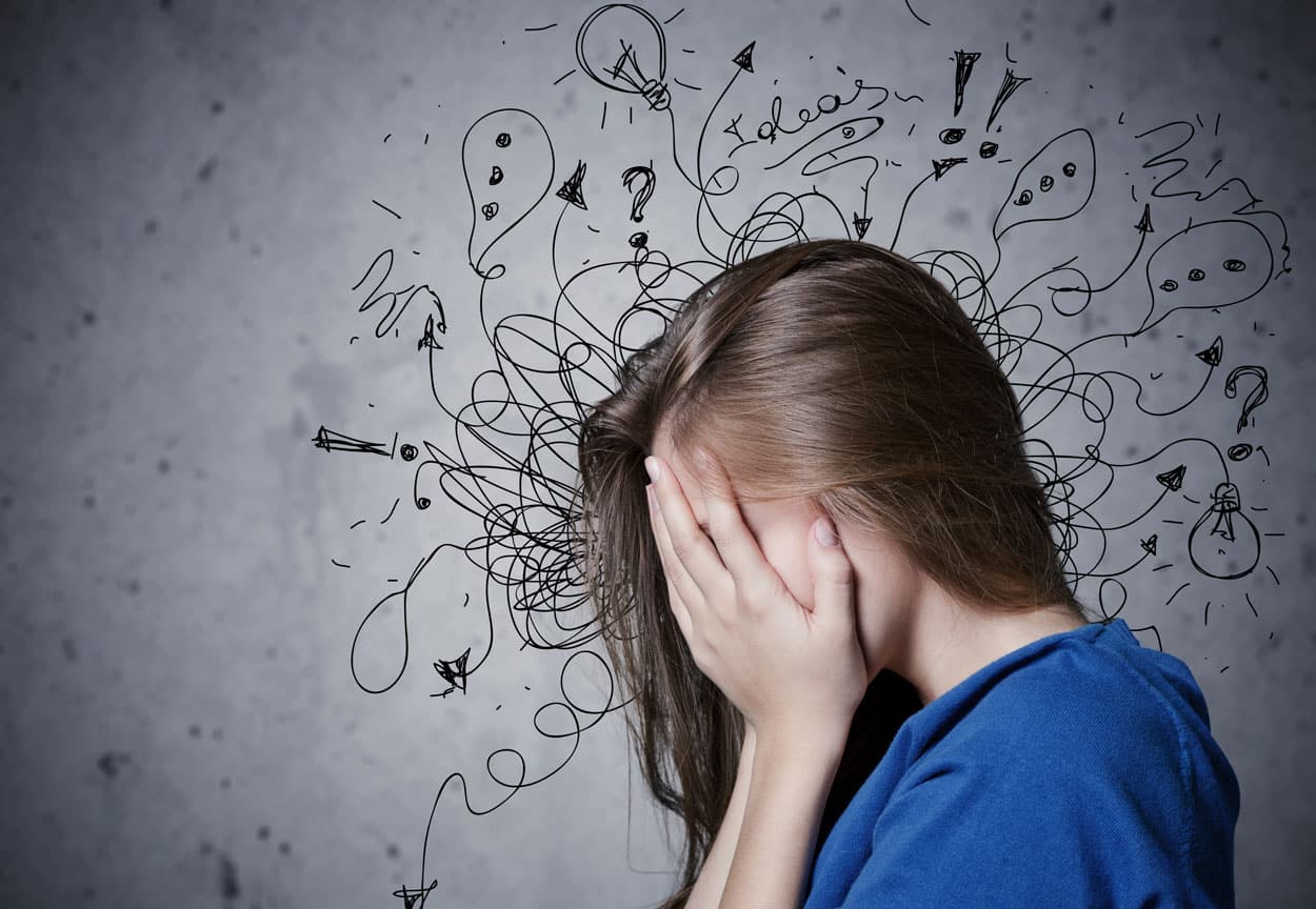 Side profile of a woman covering her face with her hands. The background is gray with messy scribbles.